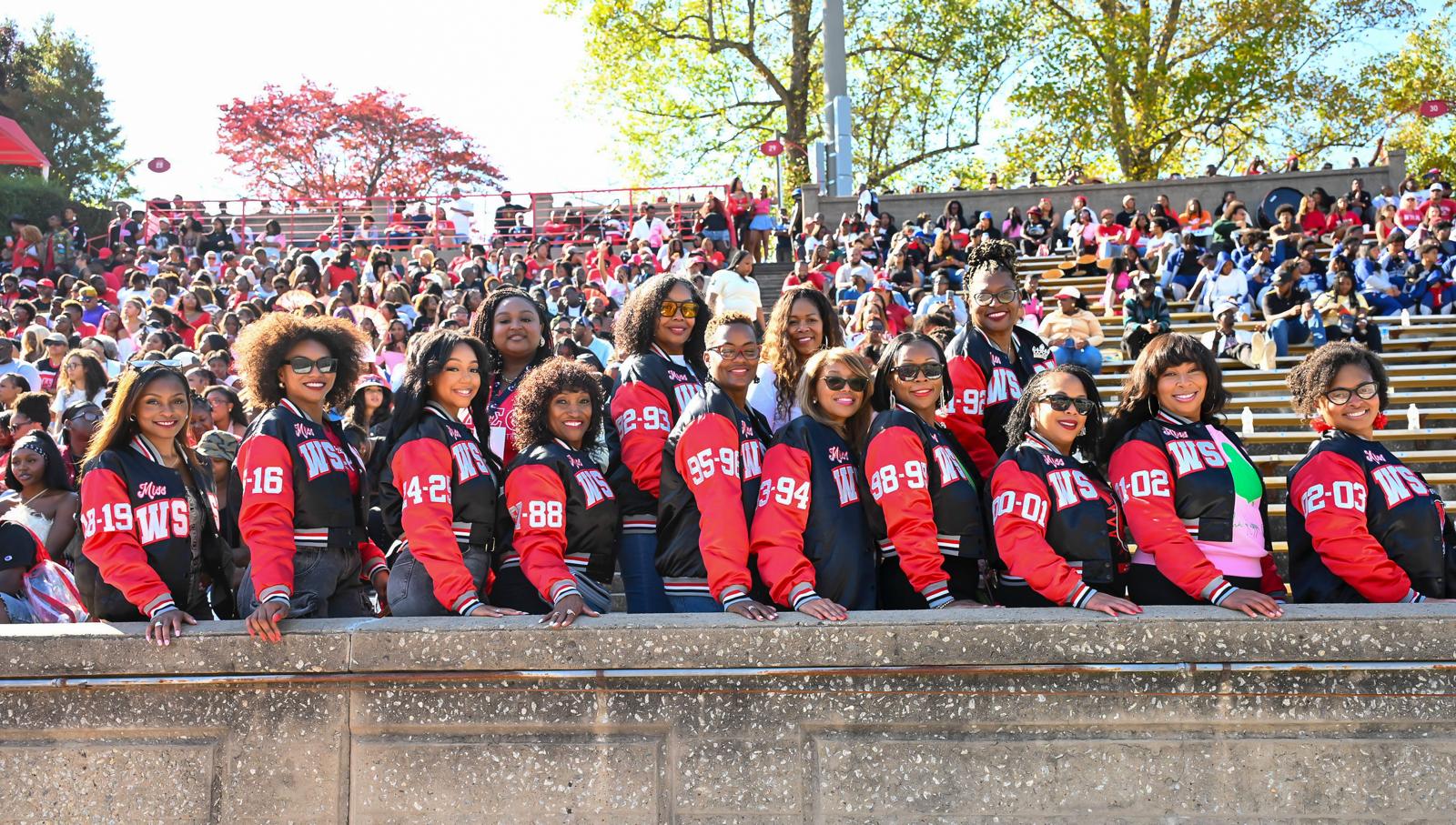Line of alumnae queens posing along the stadium wall